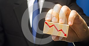 Businessman holds wooden block with red down arrow. The concept of reducing profits and income. Recession and the financial crisis