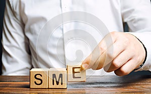 Businessman holds wooden blocks with the word SME. Small and medium-sized enterprises - commercial enterprises that do not exceed photo