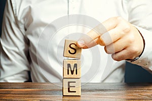 Businessman holds wooden blocks with the word SME. Small and medium-sized enterprises - commercial enterprises that do not exceed