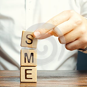 Businessman holds wooden blocks with the word SME. Small and medium-sized enterprises - commercial enterprises that do not exceed