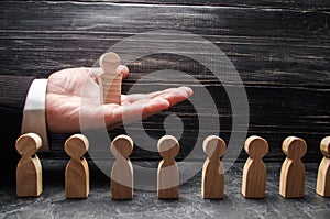 A businessman holds a wooden leader figure on the palm of his hand over a number of other workers. Concept leader, team work.