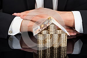 Businessman With House Made Of Currency At Desk