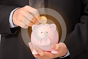 Businessman insert gold coin into piggy bank