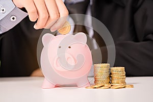 Businessman insert gold coin into piggy bank
