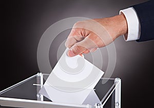 Businessman inserting ballot in box on desk