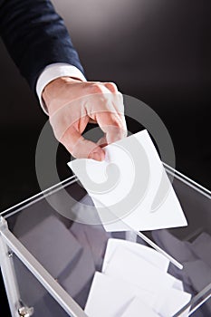 Businessman inserting ballot in box on desk