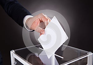 Businessman inserting ballot in box on desk photo