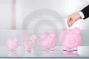 Businessman inserting coin in piggybank at office desk