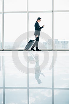 Businessman at international airport moving to terminal gate for airplane travel trip looking in phone in hand