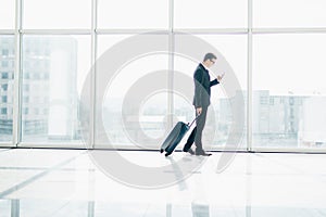 Businessman at international airport moving to terminal gate for airplane travel trip looking in phone in hand