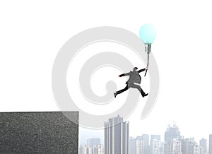 Businessman jumping from bulding top to catch glowing lamp balloon