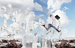 Businessman jumping over a chasm in a city, papers