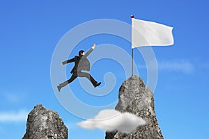 Businessman jumping over mountain peak to blank flag with sky