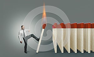 Businessman kicking a lit match to ignite a chain reaction