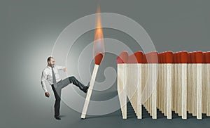Businessman kicking a lit match to ignite a chain reaction photo