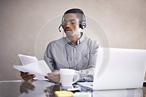 Businessman, laptop and headphones with paperwork for call center, online advice or consulting at office. Black man