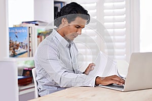 Businessman, laptop and paperwork at desk in home for remote work, research or online planning in workspace. Financial