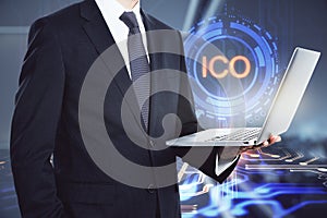 Businessman with laptop standing on ICO hologram background