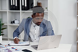 Businessman with laptop. Young African businessman is typing something on laptop in his office.