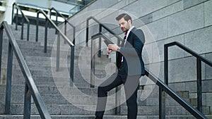 Businessman laughing with phone in hand at street. Man using smartphone outdoor