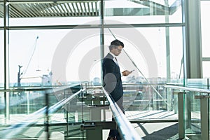Businessman leaning on railing and using mobile phone in corridor at modern office building