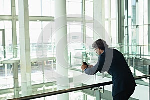 Businessman leaning on railing and using mobile phone in a modern office building