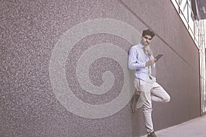 Businessman leaning on wall and holding iPod. Space for