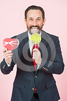 Businessman with lollipop and heart in hands. portrait of funny handsome man holding candy and opened mouth with tongue.