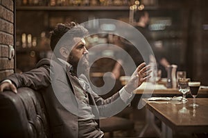 Businessman with long beard in cigar club. Confident bar customer speak in cafe. Date or business meeting of hipster in