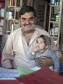 Businessman look in front smiling, hold his infant, sit at grocery shop.