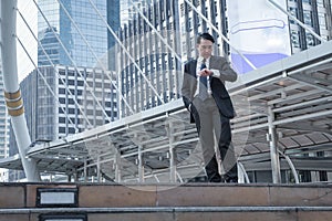 Businessman look his watch and stand on ground with modern buil