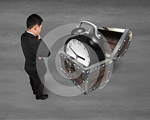 Businessman looking at alarm clock in treasure chest.