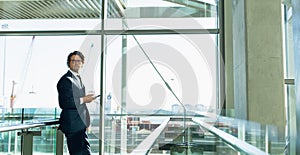 Businessman looking away while using mobile phone in corridor at modern office building