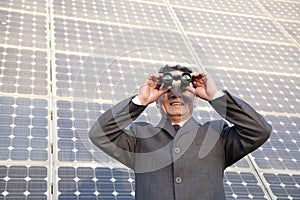 Businessman looking through binoculars in front of solar panels