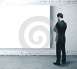 Businessman looking on blank poster on brick wall