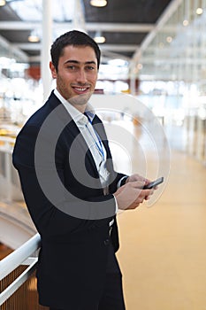 Businessman looking at camera while working on mobile phone in a modern office