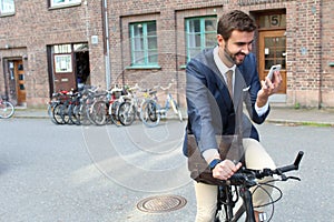 Businessman looking at this cell phone while riding a bicycle