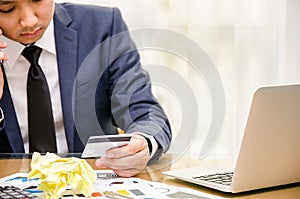 Businessman looking at the credit card in stress. Calculator accounting costs, charges, taxes and mortgage for paying bills