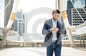 The businessman looking down at his watch and wearing deep blue suit while he waiting his friend at the outside office