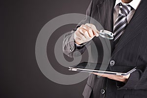 Businessman looking at his tablet through magnifying glass