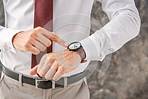 Businessman looking at his watch on grey background, closeup. Time management concept