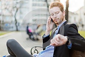 Businessman looking at his watch on a sunny day in a city park