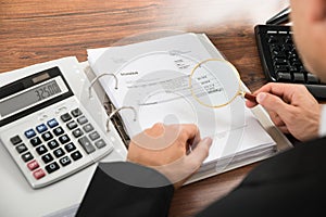 Businessman looking at invoice through magnifying glass