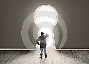 Businessman looking through a keyhole shape door