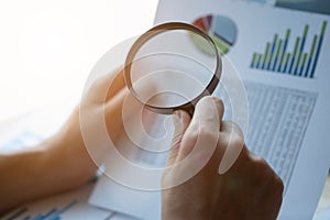 Businessman looking through a magnifying glass to documents. Business assessment and audit. Magnifying glass on a financial report