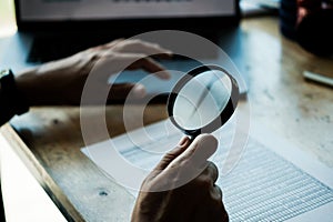 Businessman looking through a magnifying glass to documents. Business assessment and audit. Magnifying glass on a financial report