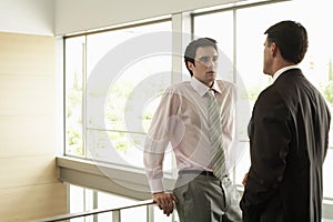 Businessman Looking At Male Colleague By Railing In Office