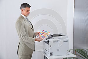 Businessman Looking At Multi Colored Paper By Color Printer