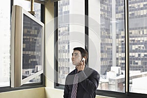 Businessman Looking At Plasma Television While Communicating On Mobile Phone