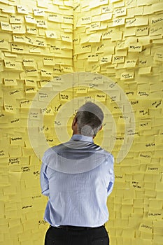 Businessman Looking At Wall Covered In Sticky Notes